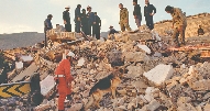 photograph of workers standing on a pile of earthquake rubble