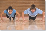 photograph of a girl and boy doing push-ups on a gym floor