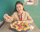 photograph of a teenage girl at a table eating from a plate of nachos