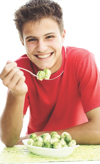 photograph of a teenage boy eating brussel sprouts