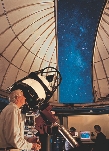 photograph of a scientist looking through a large telescope inside an obsevatory