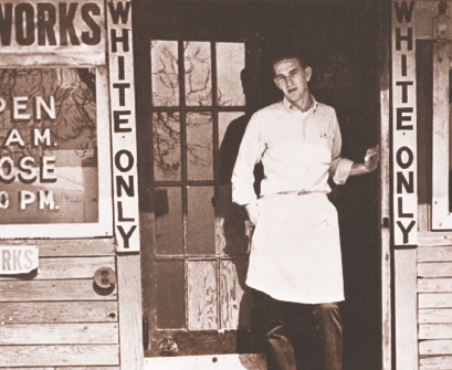 photograph of a man in front of a restaurant with signs that read “white only”