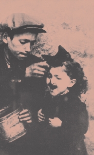 photograph of an older boy feeding a spoonful of food to a little girl