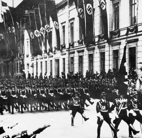 photograph of Nazi soldiers marching down a street with Nazi flags hung from windows