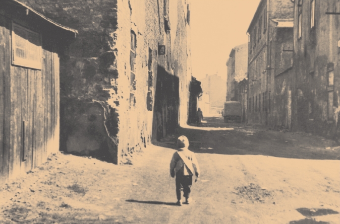 photograph of a little boy walking down a street in a deserted, ruined town