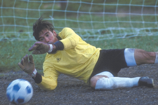 photograph of a male soccer player on the ground with a soccer ball approaching