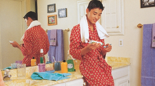 photograph of a young man in a bathroom putting toothpaste on a toothbrush