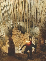 Photograph of a person in a cave with rock formations (stalactites, stalagmites)