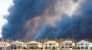 Photograph of a row of homes with black smoke from a fire in the distance