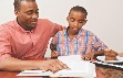 Photograph of a man helping a boy with his homework assignment