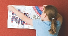 Photograph of a girl putting a poster on a wall