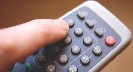 Photograph of a finger pressing a button on a remote control