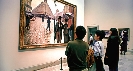 Photograph of several people looking at a painting hanging in a museum