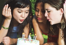 Photograph of three teenage girls blowing out candles on a cake