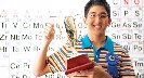 Photograph: boy with a blue ribbon and trophy, in front of the Periodic Table