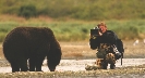 Photograph of a man with a camera very close to a bear in the wild