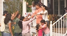 Photograph of people greeting people with hugs at the porch of a house