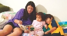 Photograph of a teenage girl reading a book to two young children