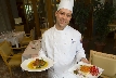 Photograph of a smiling chef holding two plates with food