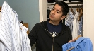 Photograph of a teenage boy by a closet holding two different shirts on hangers