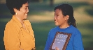 Photograph of a smiling woman and girl. Girl holds a plaque.