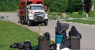 Photograph of a garbage truck approaching curbside trash cans for pick up