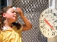 Photograph of a girl wiping her brow by a thermometer that reads over 100 degrees