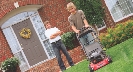 Photograph of a person mowing a lawn with another person looking on