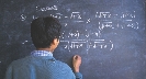 Photograph of a person at a chalkboard completing a higher order math exercise