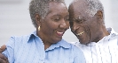 Photograph of two older adults smiling. The man has his arm around the woman.