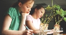 Photograph of two students writing with plants in front of each student