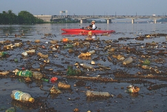 A kayaker passes by trash along the shore of the Anacostia River.