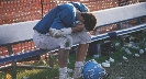 Photograph of a teen football player, bent over and sitting on a bench alone