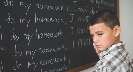 Photograph of a boy standing in front of a chalkboard with writing