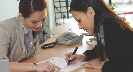 Photograph of a woman pointing to a piece of paper as another woman signs it