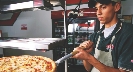 Photograph of someone putting pizza into an oven at a pizza parlor