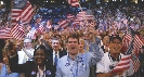 Photograph of a crowd of people, some of whom are holding U.S. flags