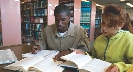 Photograph of two people at a library with opened books in front of them