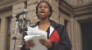 Photograph of a young woman speaking into a microphone at a public place