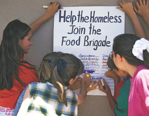 Photograph of students writing their names on a sign-up poster about helping the homeless