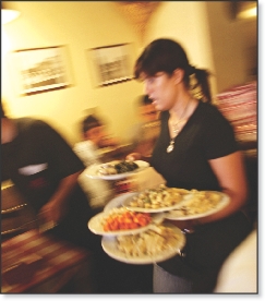 Photograph of a restaurant worker moving quickly with several plates balanced on her arm