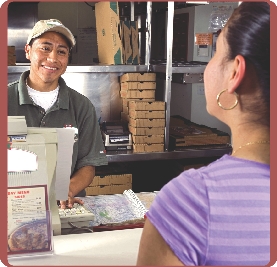 Photograph of a worker behind the counter at a restaurant that serves pizza