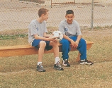 Photograph of two boys sitting on a bench, one holds a soccer ball