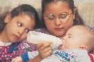 Photograph of baby being bottle-fed by an older girl as younger girl looks on