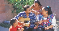 Photograph of two adults and two children singing as male adult plays guitar