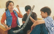 Photograph of a girl frightened by a fake snake as two boys sit and laugh