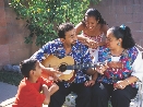 Photograph of two adults and two children singing as male adult plays guitar