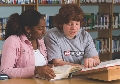 Photograph of two women at a library reading from the same book