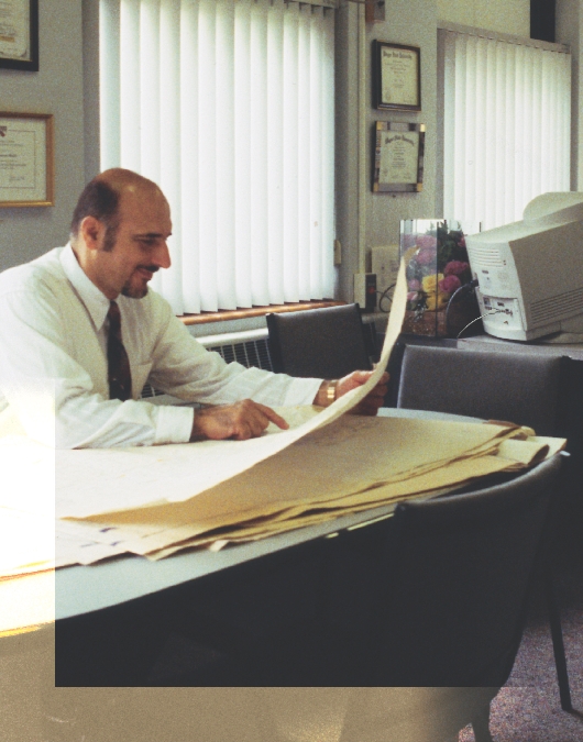 photograph of an adult man (Hassan) seated at a desk in an office