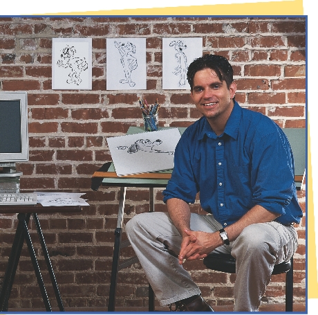 photograph of man sitting next to desk with sketches of cartoon character dog on the wall behind him